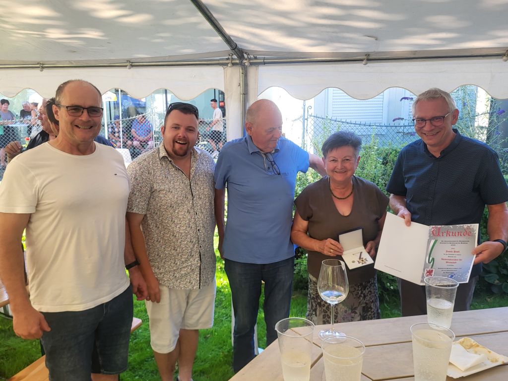 Fünf Personen stehen unter einem Zelt, eine Frau erhält Urkunde und Medaille.